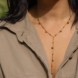 A person in a beige collared shirt wears the Dax Lariat Necklace by Peter and June, a delicate 18k gold plated piece with small round beads, photographed from the shoulders up.
