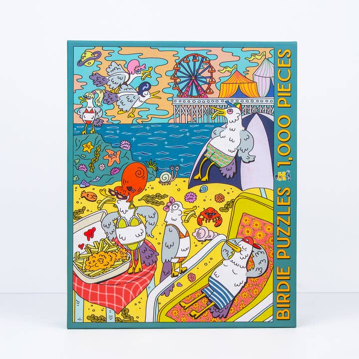 Colorful 1000-piece jigsaw puzzle by Birdie Puzzles, titled "Gull Trouble," features quirky cartoon birds at the beach with a ferris wheel, boardwalk, and ocean. Made from recycled materials, this fun puzzle is perfect for bird lovers.
