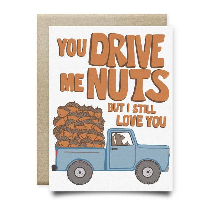 The Drive Me Nuts Card by Anvil Cards features a hand-drawn dog driving a blue truck filled with acorns on sustainable linen paper, with the message: "You drive me nuts but I still love you.