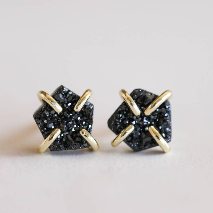 The JaxKelly Druzy Prong - Black Earrings feature pentagon-shaped black druzy stones in gold prong stud settings. Hypoallergenic and tarnish free, these earrings are perfect for sensitive ears.