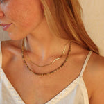 Woman wearing Token Jewelry’s Dune Beaded Necklace and a wavy gold fill necklace—handmade pieces—shown from the shoulders up against a neutral background.