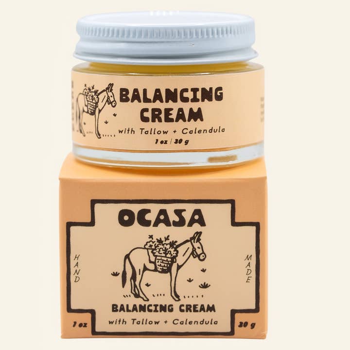 A small jar of Calendula Tallow Face Cream | OCASA resting on its matching square box, both featuring a donkey with flowers and labels for this tallow moisturizer with calendula.