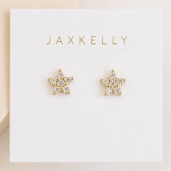 A pair of Pave Stud Flower earrings by JaxKelly, featuring sparkling white CZ gemstones set in a delicate floral design with durable gold plating. Displayed on a white card labeled “JaxKelly,” these hypoallergenic studs are ideal for sensitive ears.