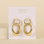 A pair of JaxKelly Gold Hoop Coupled earrings are displayed on a white "JaxKelly Wear Good Vibes" card against a beige background.