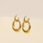 The JaxKelly Earrings | Gold Hoop Coupled feature thick, rounded 18kt gold bands, shown against a neutral beige background.
