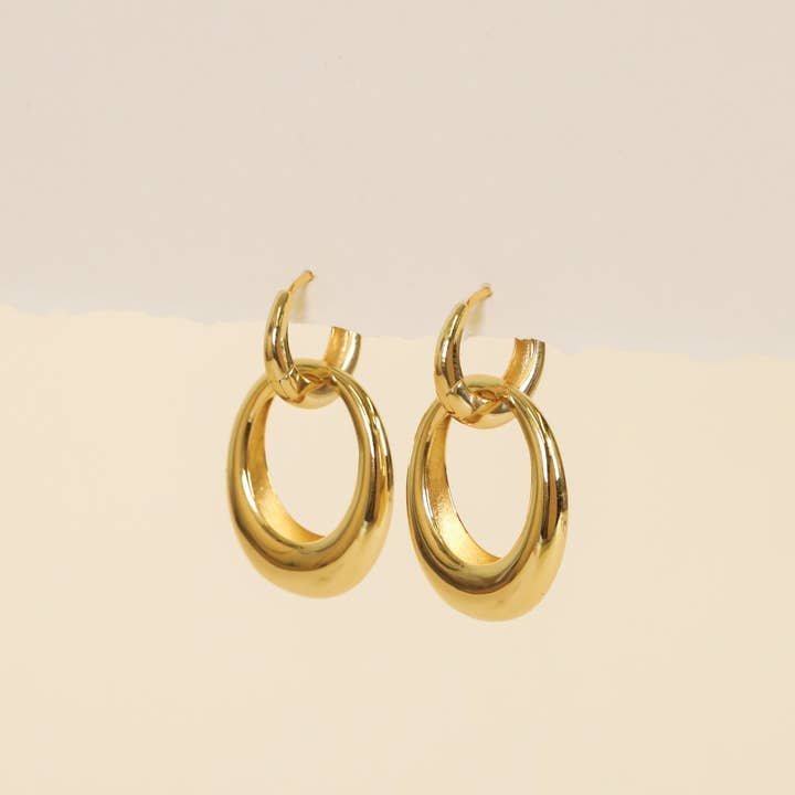 A pair of Gold Hoop Coupled Earrings by JaxKelly, crafted in 18kt gold, displayed against a neutral beige background.