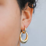 Close-up of a person's ear wearing JaxKelly's Gold Hoop Coupled Earrings, featuring double 18kt gold hoops. The lightweight earrings stand out against short curly hair and a neutral backdrop.