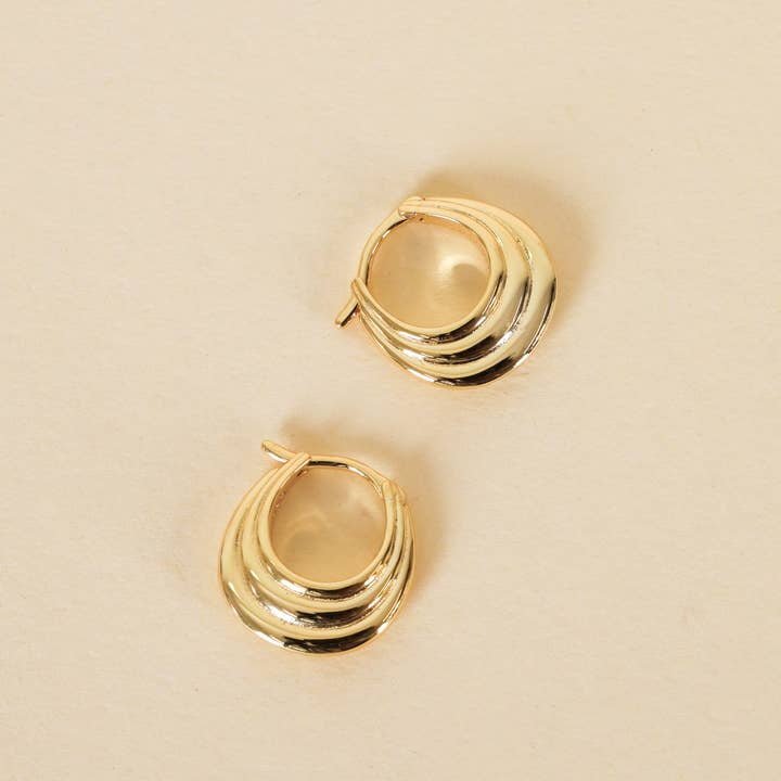 JaxKelly Gold Hoop - Triple Arch Earrings feature a layered, wavy design and 18K gold plating, showcased on a neutral beige surface.