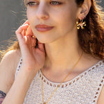 A woman wearing a sleeveless crochet top, Knotty Hoops earrings by Peter and June, and a matching butterfly necklace.