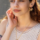 A woman wearing a sleeveless crochet top, Knotty Hoops earrings by Peter and June, and a matching butterfly necklace.