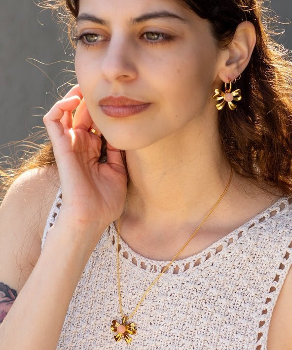 A woman wearing a sleeveless crochet top, Knotty Hoops earrings by Peter and June, and a matching butterfly necklace.