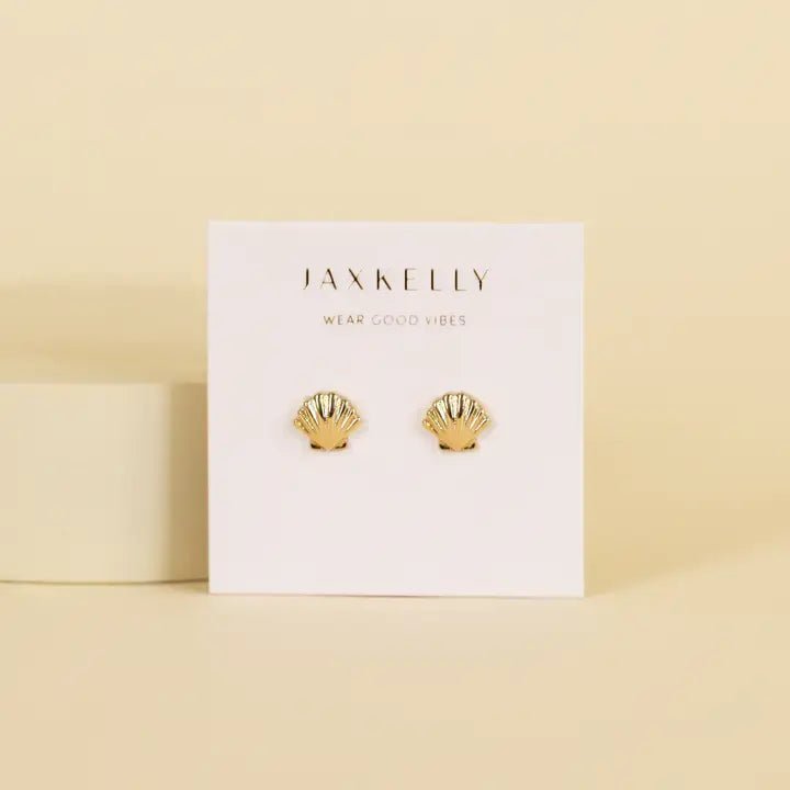 A pair of hypoallergenic gold seashell stud earrings from JaxKelly, shown on a white card featuring the "Wear Good Vibes" message.