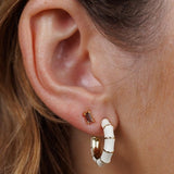 Close-up of a person's ear wearing two earrings: a small rectangular stud and a larger JaxKelly Vintage Hoop earring.