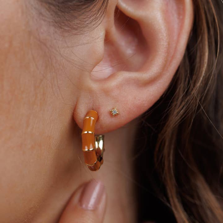Close-up of a person’s ear adorned with JaxKelly Vintage Hoop and gold stud earrings, both hypoallergenic and perfect for sensitive skin. A hand gently touches the neck below.