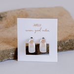 A pair of wide hoop earrings by JaxKelly, displayed on a branded card that reads "wear good vibes," set against a stone background.