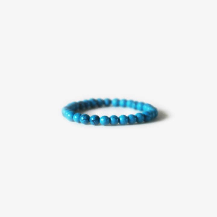 The Earth Bracelet - Blue Howlite by BRANCO features small, round blue beads arranged in a circle and is shown against a plain white background.