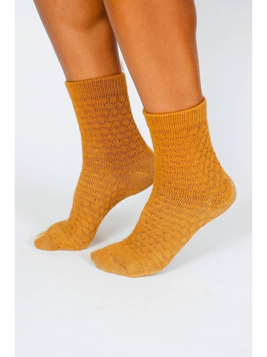 A person wearing Tailored Union’s Eben Ankle Sock in mustard yellow, standing on a white surface.