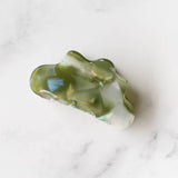 The Eco Cloud Hair Claw Clip | Tiepology—by Tiepology—features a chic green and white marbled, cloud-shaped design. Resting on white marble, this stylish and eco-friendly accessory is perfect for any occasion.