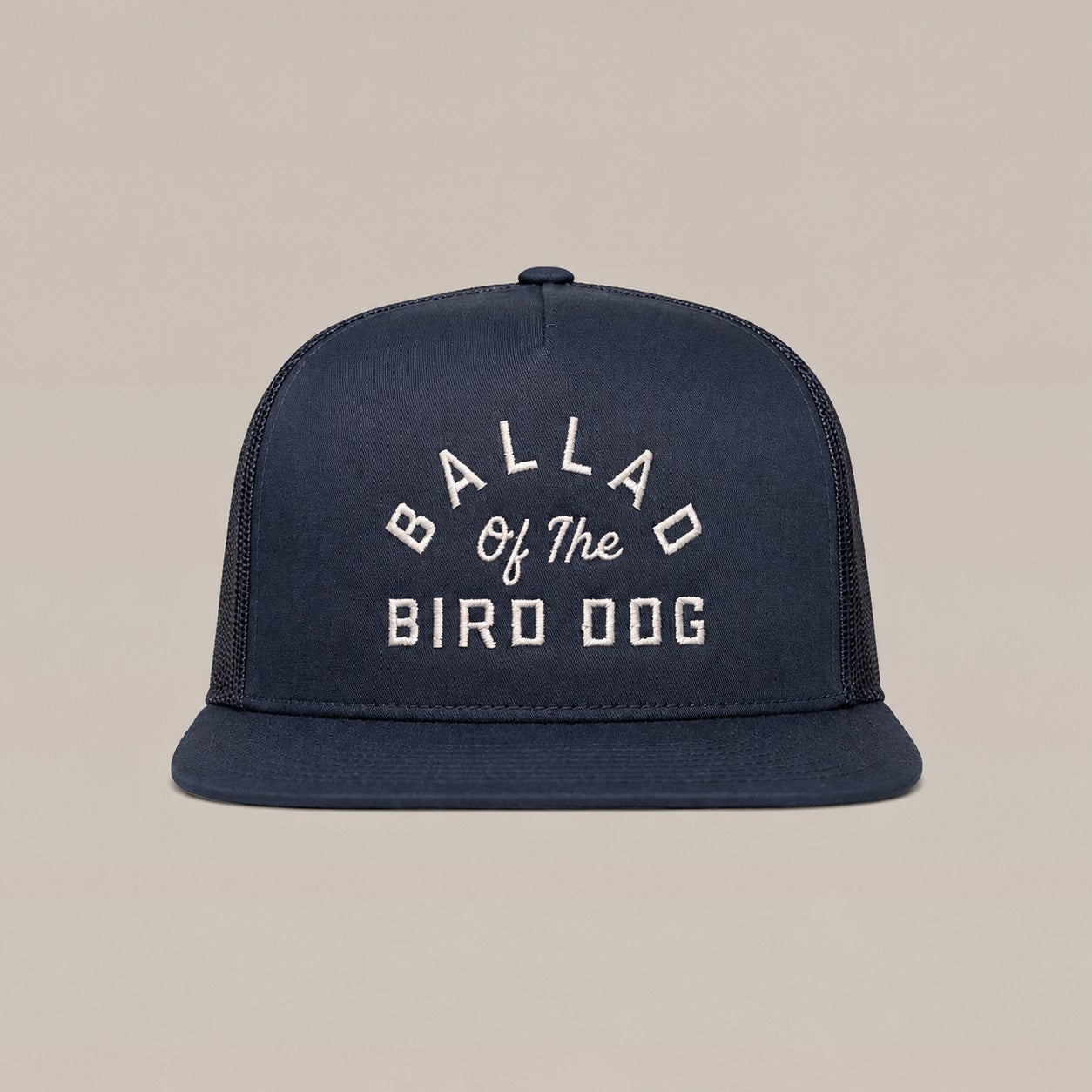 The Arch Logo Hat by Ballad Originals is a navy blue trucker cap featuring a stylish arch logo and white embroidered “BALLAD OF THE BIRD DOG” text on the front, showcased against a plain beige background.