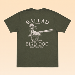Olive green illustrative Roadrunner vs. Rattlesnake t-shirt by Ballad Originals, featuring a bird graphic and the text “BALLAD of the BIRD DOG Trust Your Gut” on the back, displayed flat on a tan background.
