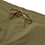 Close-up of Howler Brothers Electrolight Tech Pants in olive green, featuring a front pocket and a tan drawstring tied at the waistband.