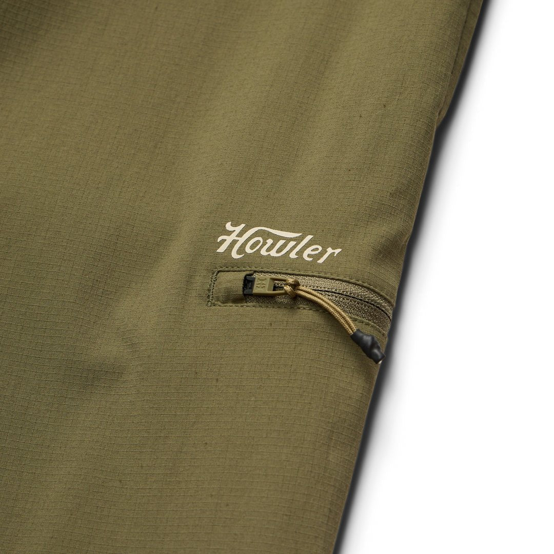 Close-up of an olive green nylon ripstop pocket with a zipper and "Howler" printed in white above, from the Electrolight Tech Pants by Howler Brothers.
