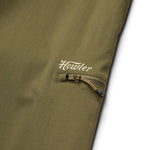 Close-up of an olive green nylon ripstop pocket with a zipper and "Howler" printed in white above, from the Electrolight Tech Pants by Howler Brothers.