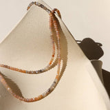 The Ember Moonstone Necklace by Token Jewelry, featuring small round pastel-colored stones, is draped over the edge of a textured off-white ceramic dish.