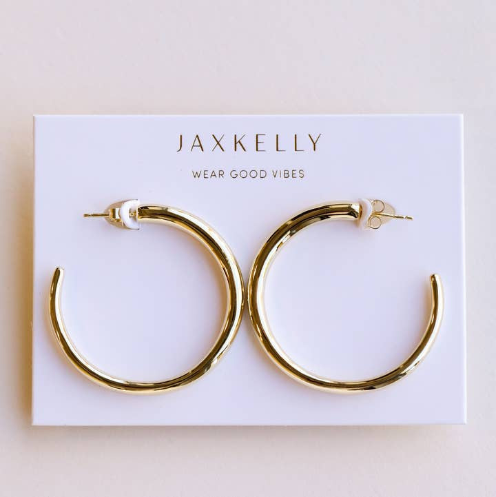 The JaxKelly Everyday Gold Hoop Earrings are bold, tarnish-free hoops displayed on a white card featuring the message "Wear Good Vibes.