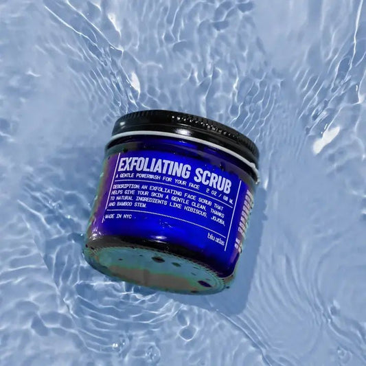 A blue jar labeled "Exfoliating Scrub | Blu Atlas" sits on rippled water, displaying the product name and usage instructions on the front.