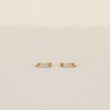A pair of Double Champagne Hoop earrings by JaxKelly, featuring small gold double hoops adorned with two rows of shimmering pave stones, displayed against a plain beige background.