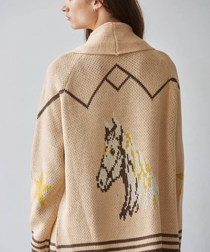 A person viewed from behind is wearing the By Together Knit Sweater Cardigan Top, a beige knit sweater featuring brown geometric patterns, jacquard detailing, and a horse design on the back.