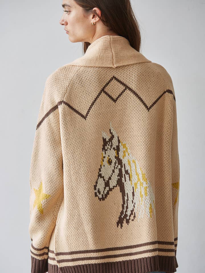 A person viewed from behind is wearing the By Together Knit Sweater Cardigan Top, a beige knit sweater featuring brown geometric patterns, jacquard detailing, and a horse design on the back.