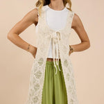 A woman wears the Sadie And Sage Fell For You Crochet Front Tie Cardigan over a white top and light green wide-leg pants, standing against a beige background—ideal for small size women’s collections.