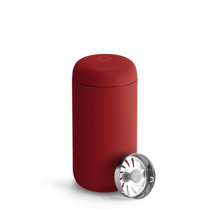 A red Fellow Carter Move Travel Mug with a matching lid is displayed next to a removable stainless steel strainer or infuser.