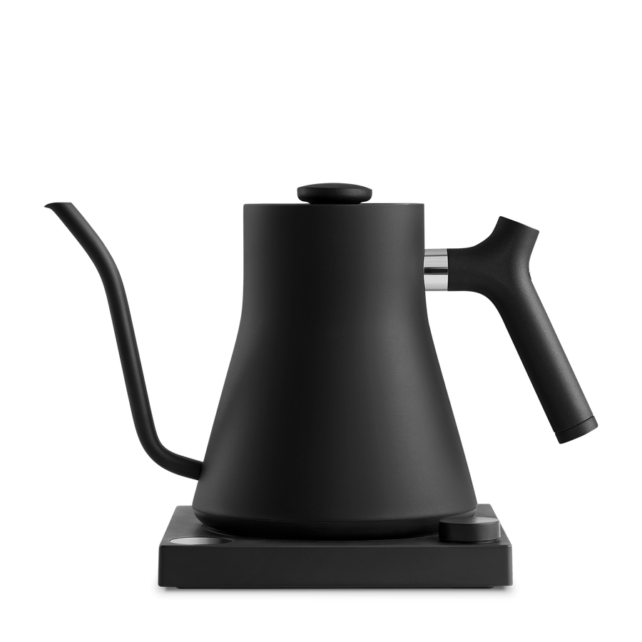 The Fellow Electric Kettle features a matte black finish, precision pour spout, and curved design on a rectangular base, showcased against a white background.