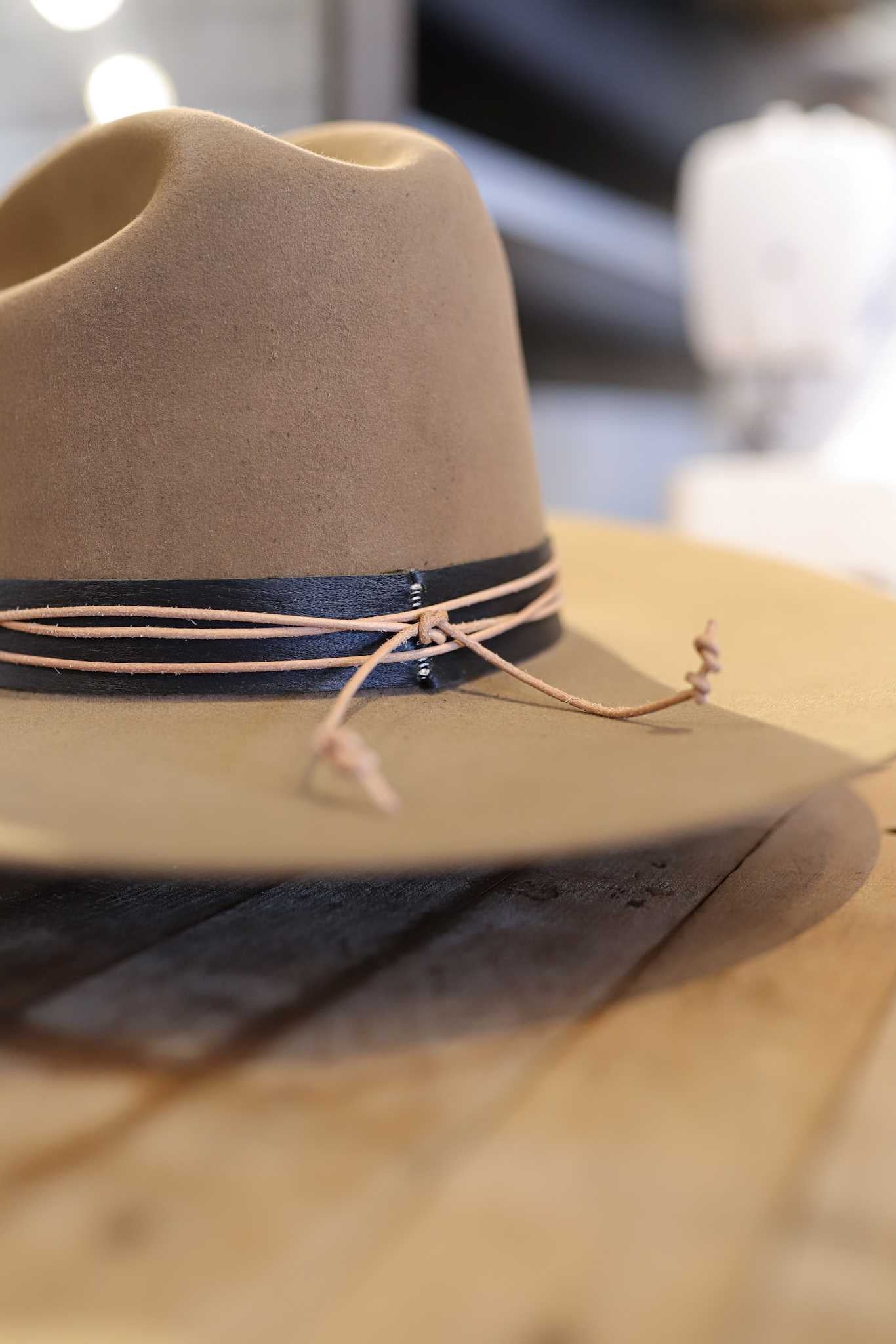 The Easy Drifter Felt Hat | Classic Cowboy features a brown felt design with a black band and tan leather cord, resting on wood and showcasing a classic western brim.