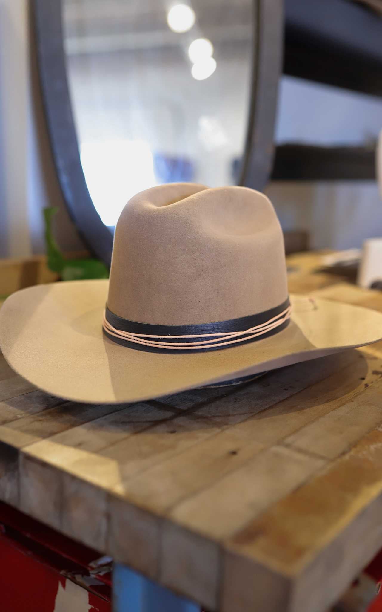 The Easy Drifter Felt Hat | Classic Cowboy, featuring a western brim and a black and pink striped band, sits on a wooden surface indoors.