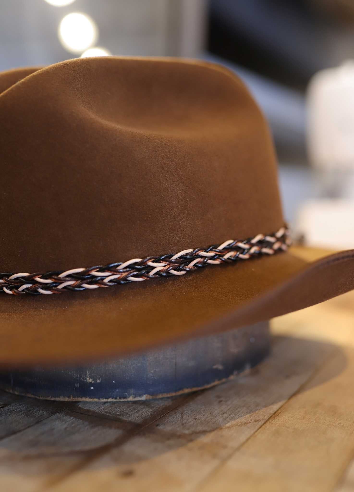 The Easy Drifter Felt Hat | Whiskey LBJ sits on a wooden surface, showcasing its classic LBJ-inspired style and braided band.