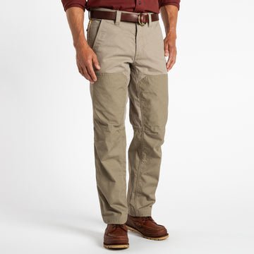 A man wearing Duck Head’s Field Canvas Briar Pant with reinforced knees, a brown belt, maroon shirt, and brown leather boots stands against a white background.