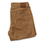 A folded pair of Duck Head Field Canvas Five-Pocket pants in brown stretch canvas, featuring a back pocket and leather waistband patch, displayed on a plain light background.