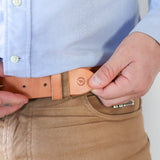 A person in a light blue shirt and tan pants fastens the Ballad of the Bird Dog Field Duty Belt, showing its subtle stamped logo, while silver rings adorn their left hand.