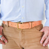 A person wearing a light blue button-up shirt, tan pants, and the Field Duty Belt by Ballad of the Bird Dog with a gold buckle, along with several rings on both hands.