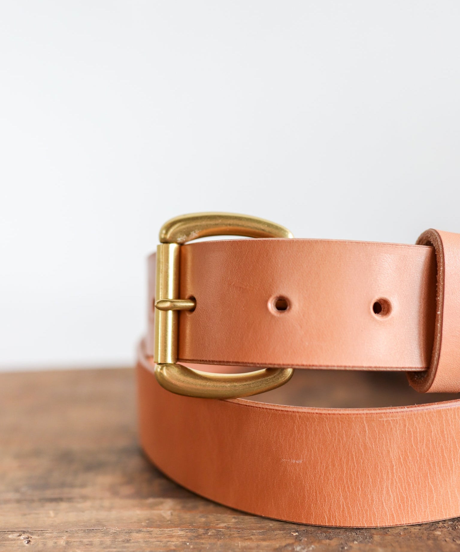 A close-up of the Ballad of the Bird Dog Field Duty Belt, featuring a gold buckle and vegetable tanned Wickett & Craig harness leather, shown resting on wood against a plain white background.