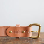 A close-up of the Ballad of the Bird Dog Field Duty Belt with a brass buckle, stamped with "Bradley Mountain" and "40", resting on a wooden surface.