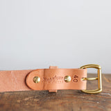 A close-up of the Ballad of the Bird Dog Field Duty Belt, featuring embossed branding and the number 40 on Wickett & Craig harness leather with a brass buckle, resting on a wooden surface.