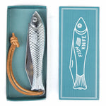 The Fingerling Fish Knife by Mollyjogger features a silver chrome, fish-shaped handle and leather strap, displayed beside its teal "Fish Knife" box with fish art—an eye-catching cutlery piece.