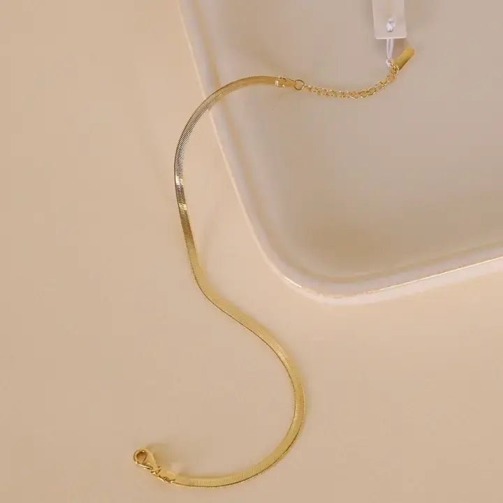 The Flat Chain Anklet - 18k Gold Plated by JaxKelly, featuring a lobster clasp and adjustable extension, is shown on a beige surface—perfect as an anklet or bracelet for versatile, tarnish-free styling.