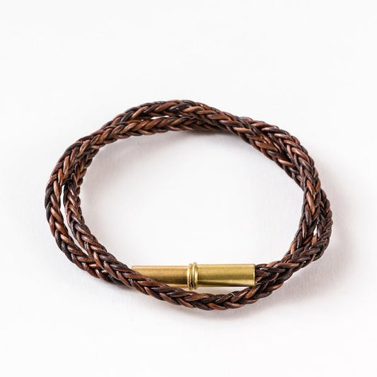 The Flint Braided Bracelet by Tres Cuervos features upcycled .22 shells and a magnetic clasp, shown coiled on a white background.