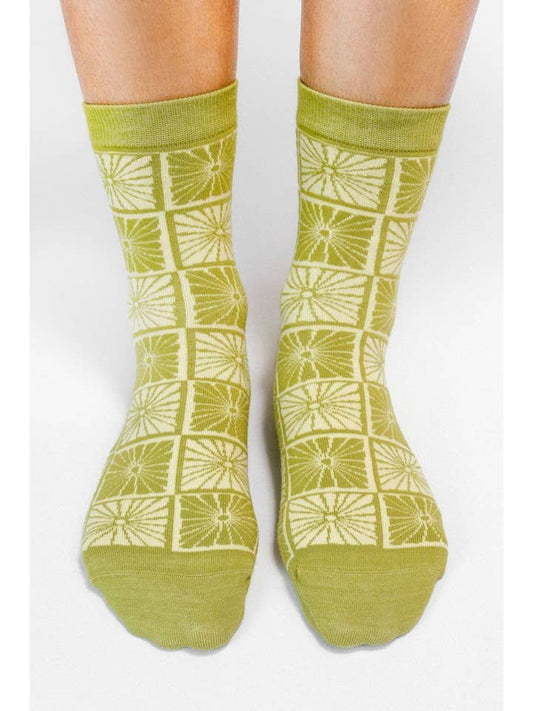 A pair of feet wearing the Tailored Union Flower Checkers Knit Ankle Sock, featuring a cream geometric square and starburst pattern inspired by Natalia Skeba art on a white background.